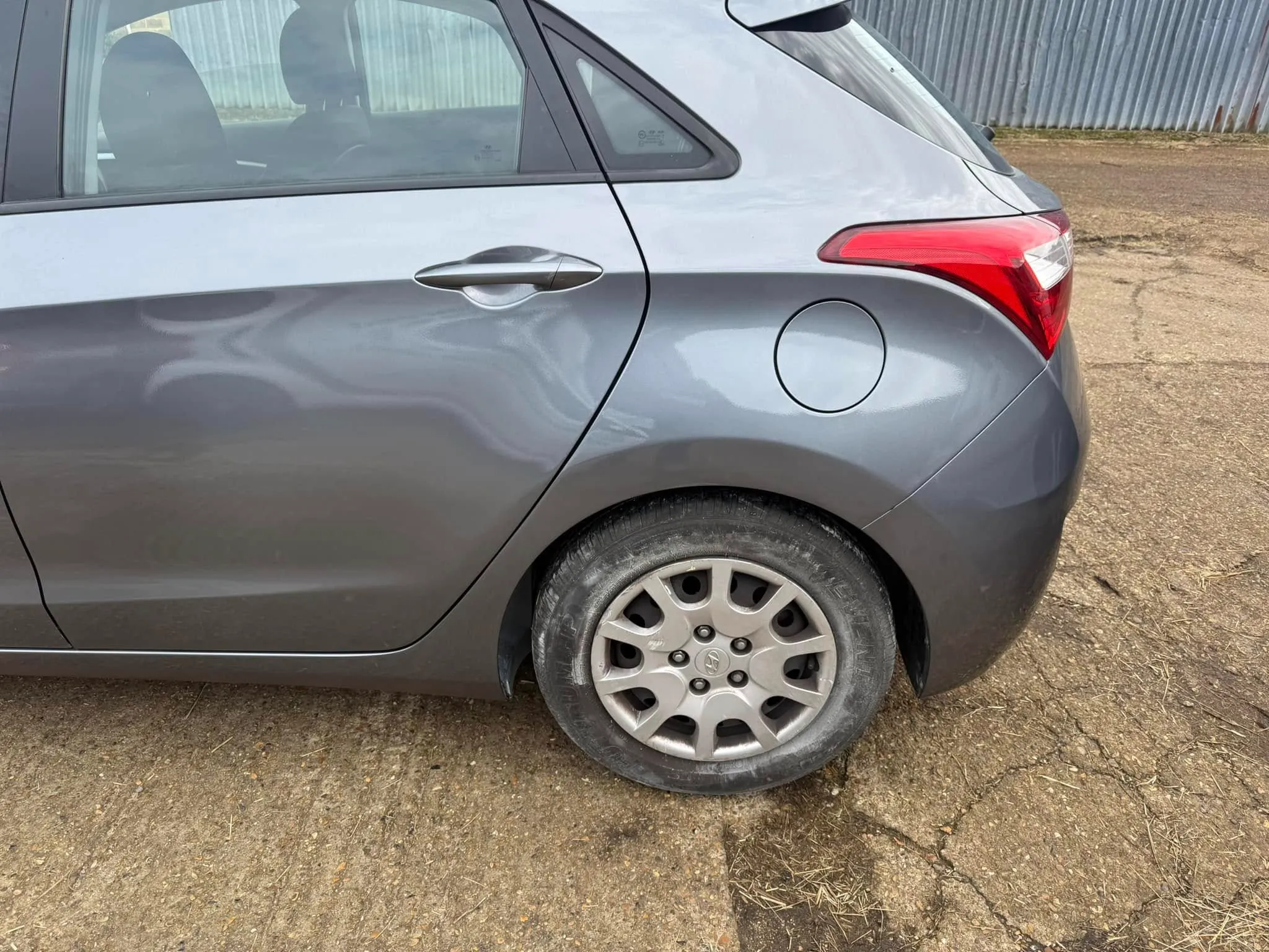 A small gray car parked in a dirt lot.